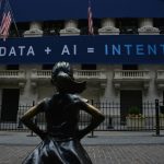 Statute of a girl standing in front of a building with a sign reading Data + AI = Intent