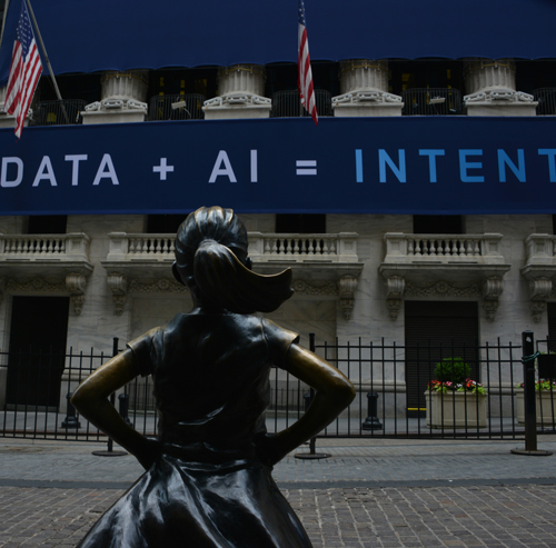 Statute of a girl standing in front of a building with a sign reading Data + AI = Intent